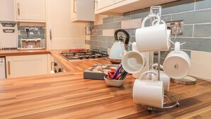 A modern kitchen with white cabinets, a wooden countertop, a gas stove, and a kettle. - Glebe Hall Apartment (Redcar)