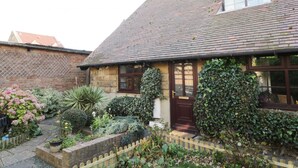 A traditional stone house with a tiled roof, a wooden door, and a small garden with various plants and a wooden fence. - Glebe Hall Apartment (Redcar)