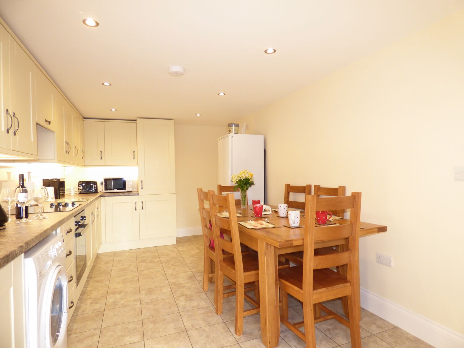 A compact kitchen with a dining area, featuring a washing machine, microwave, and a refrigerator.