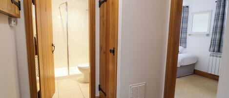 Un pasillo con una puerta de madera que da a un baño con ducha e inodoro.