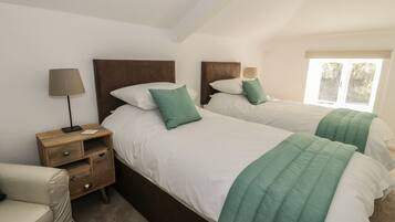 A hotel room with two single beds, a nightstand with a lamp, a bedside table, and a chair.