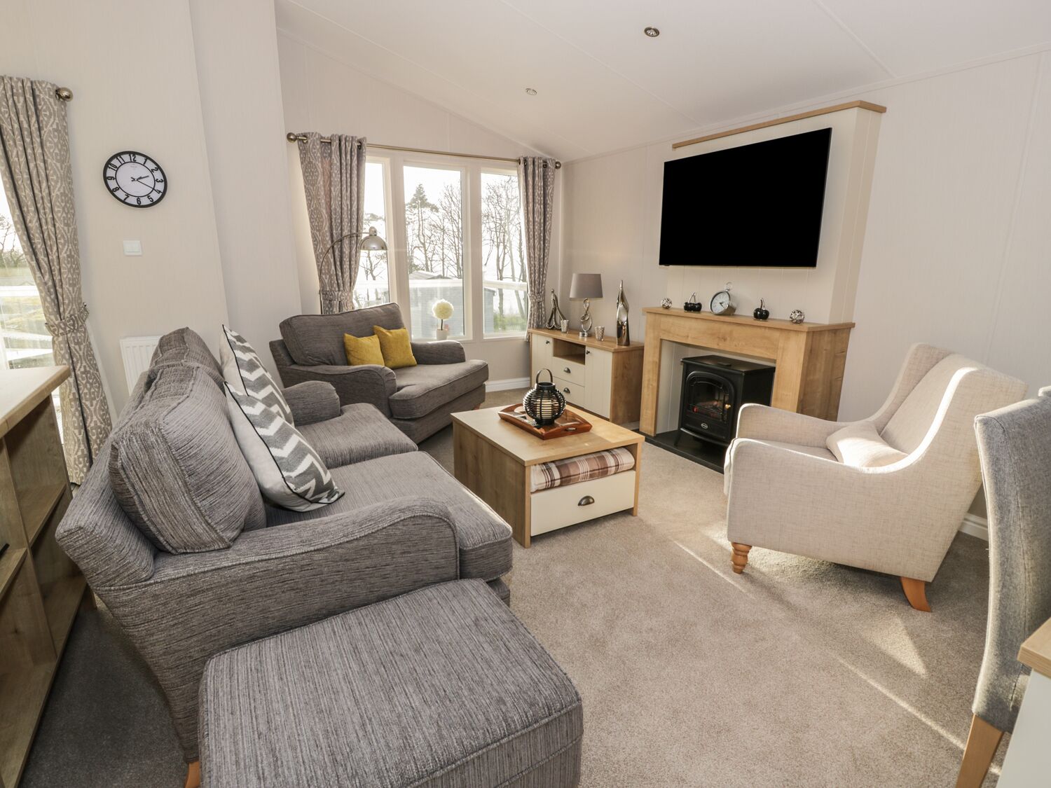 A living room with a sofa, armchair, coffee table, fireplace, TV, and large windows.