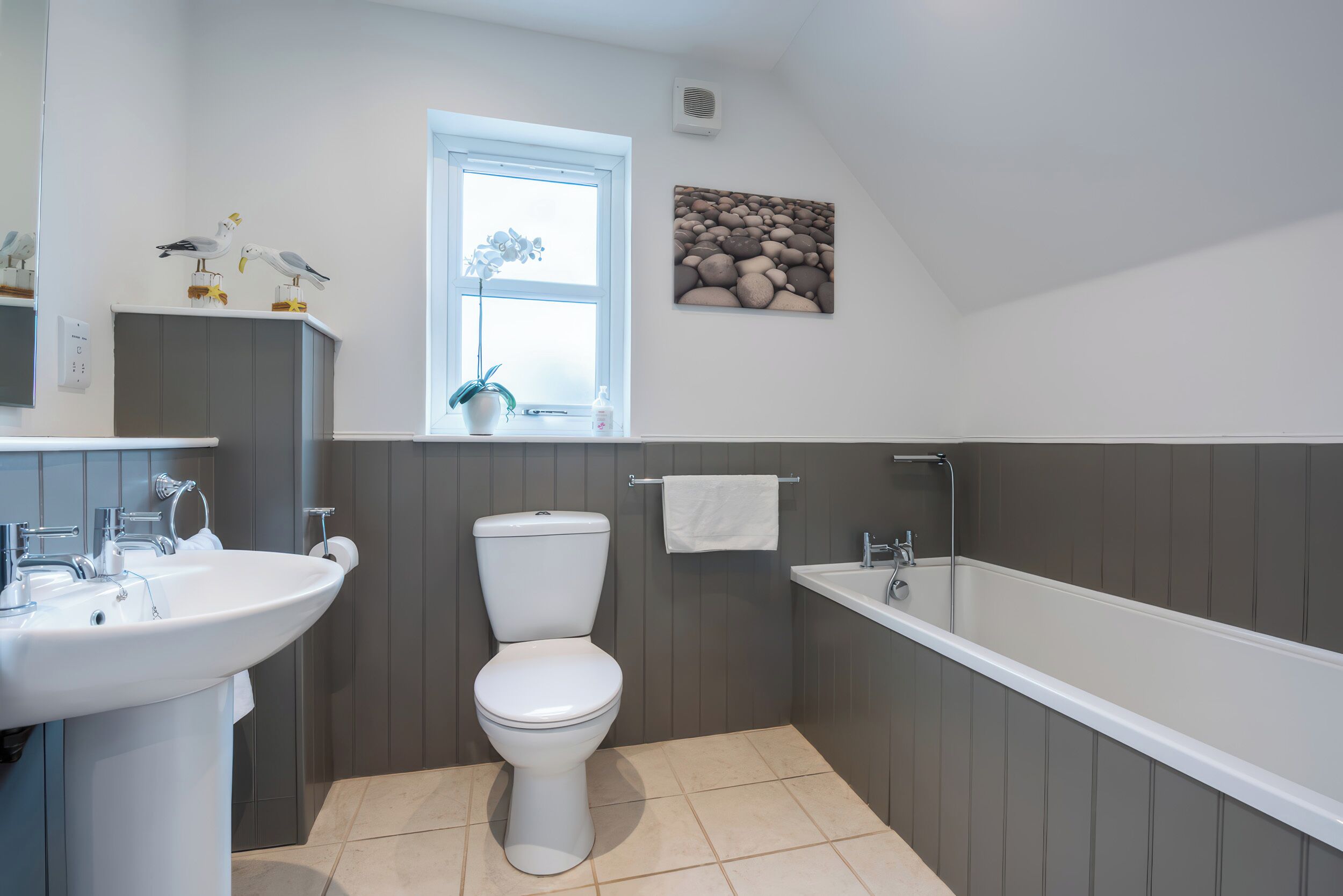 A bathroom with a white sink, toilet, and bathtub, a window with a view, and a decorative wall piece.