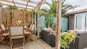 Um deck de madeira com pérgola, móveis de vime e plantas em vasos.