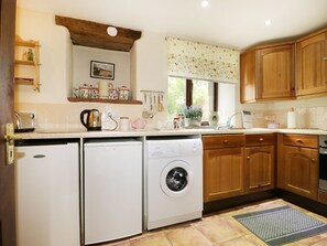 A compact kitchen with a washing machine, a coffee maker, and wooden cabinets. - Rosegarth Cottage (Penrith)