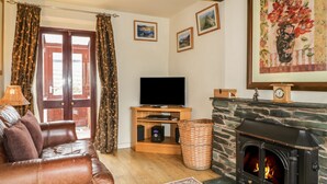 Una sala de estar acogedora con un sofá de cuero, un televisor de pantalla plana, una chimenea de piedra y un ventanal con cortinas.