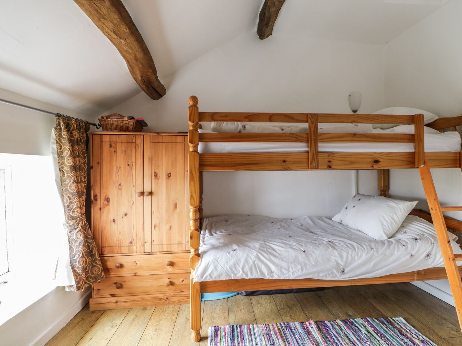 Un lit superposé avec une tête de lit en bois, une armoire en bois et une fenêtre avec des rideaux.