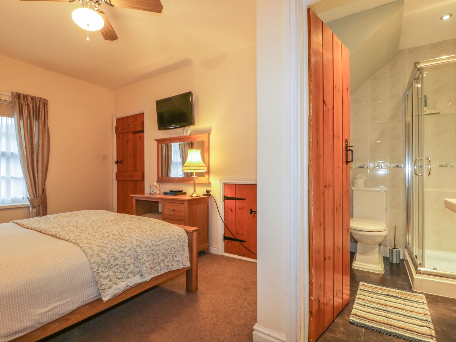 Een slaapkamer met een bed, een bureau, een televisie en een badkamer met douche en toilet.