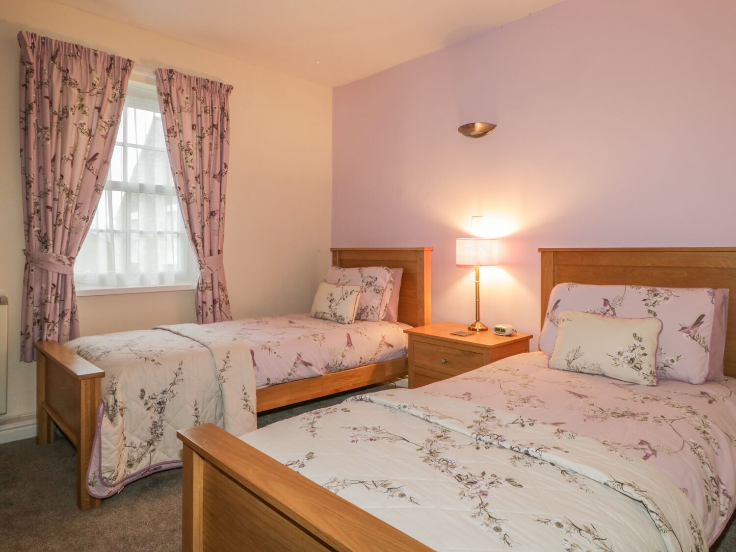 A bedroom with two single beds, a nightstand with a lamp, and a window with floral curtains.