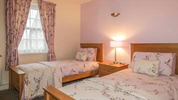 A bedroom with two single beds, a nightstand with a lamp, and a window with floral curtains.
