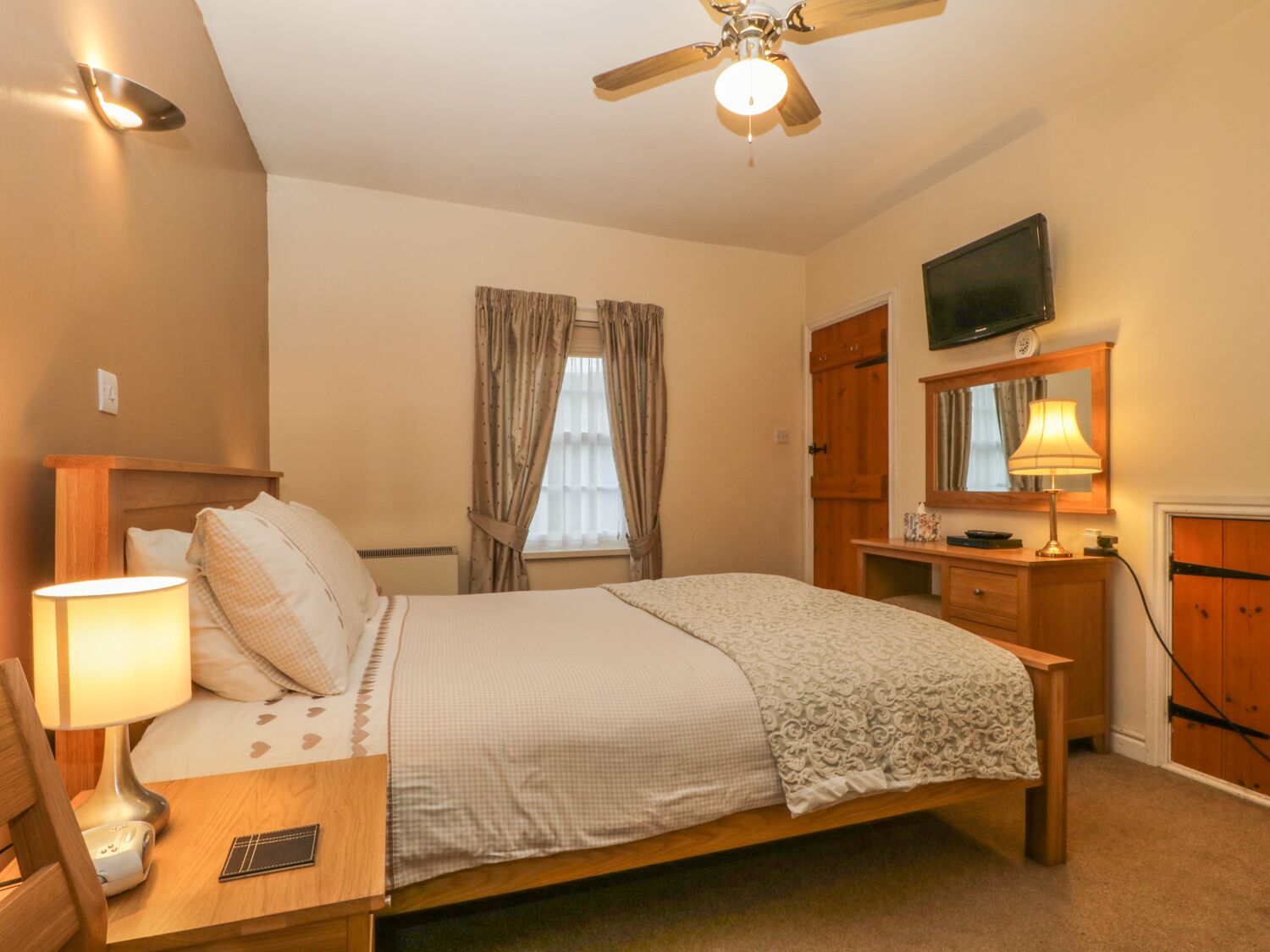 A bedroom with a bed, bedside table, lamp, TV, wardrobe, and a ceiling fan.