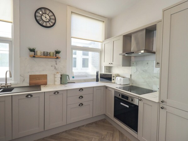 Een moderne keuken met een ingebouwde oven, magnetron en broodrooster, een spoelbak en een klok aan de muur.