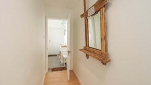 A hallway with a wooden-framed mirror on the wall, a white door at the end, and a small wooden bench. - St Johns View (Keswick)