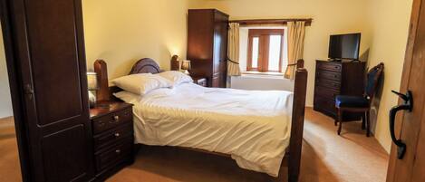 Un dormitorio con una cama grande, un armario de madera, una cómoda, una silla y un televisor.