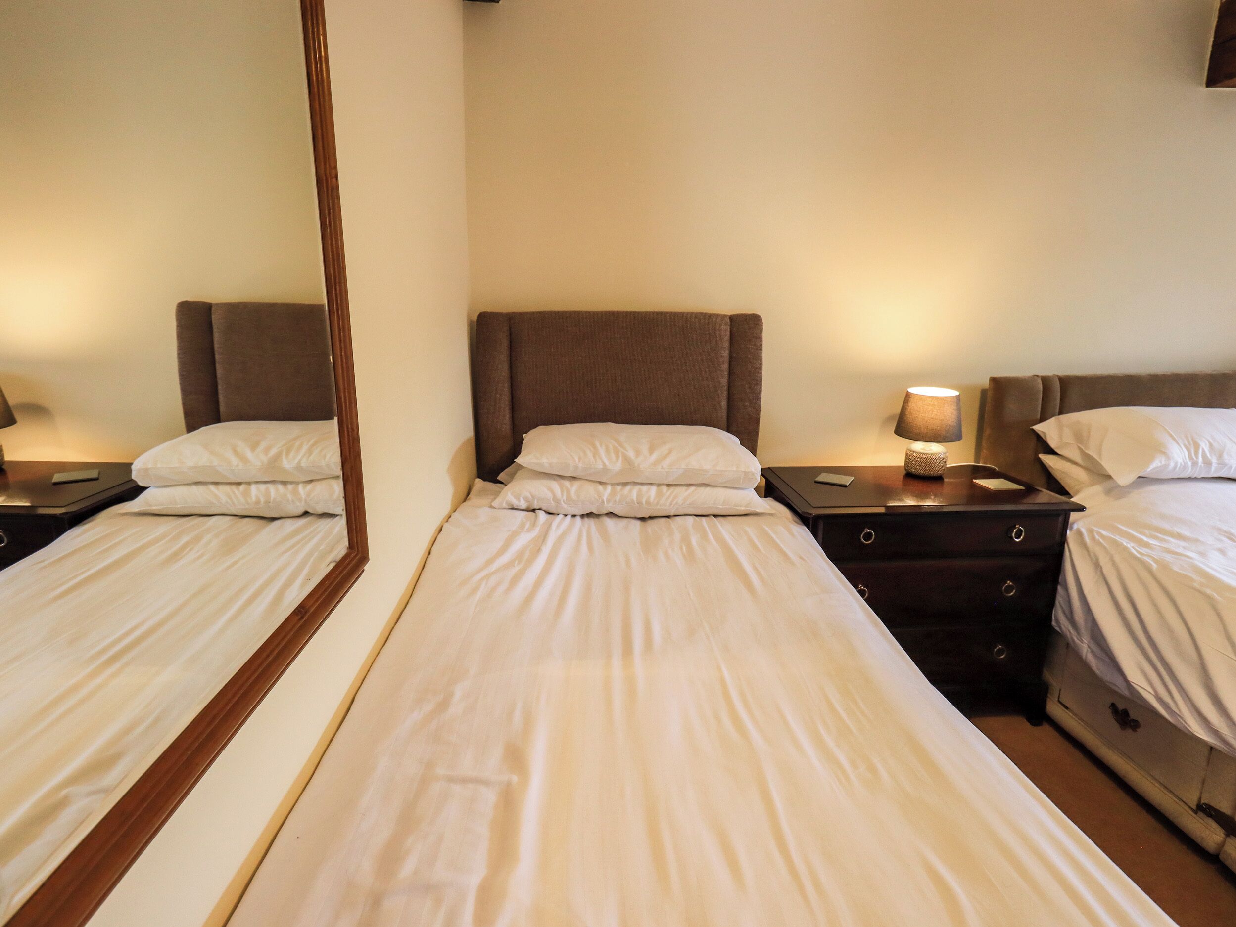 A hotel room with two single beds, each with a headboard, bedside tables, and lamps.