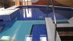 An indoor swimming pool with blue tiles, a diving board, and a tiled floor. - Waterhead Apartment F (Ambleside)