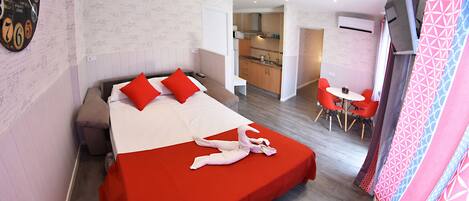 A hotel room with a large bed, a kitchenette, and a dining area.