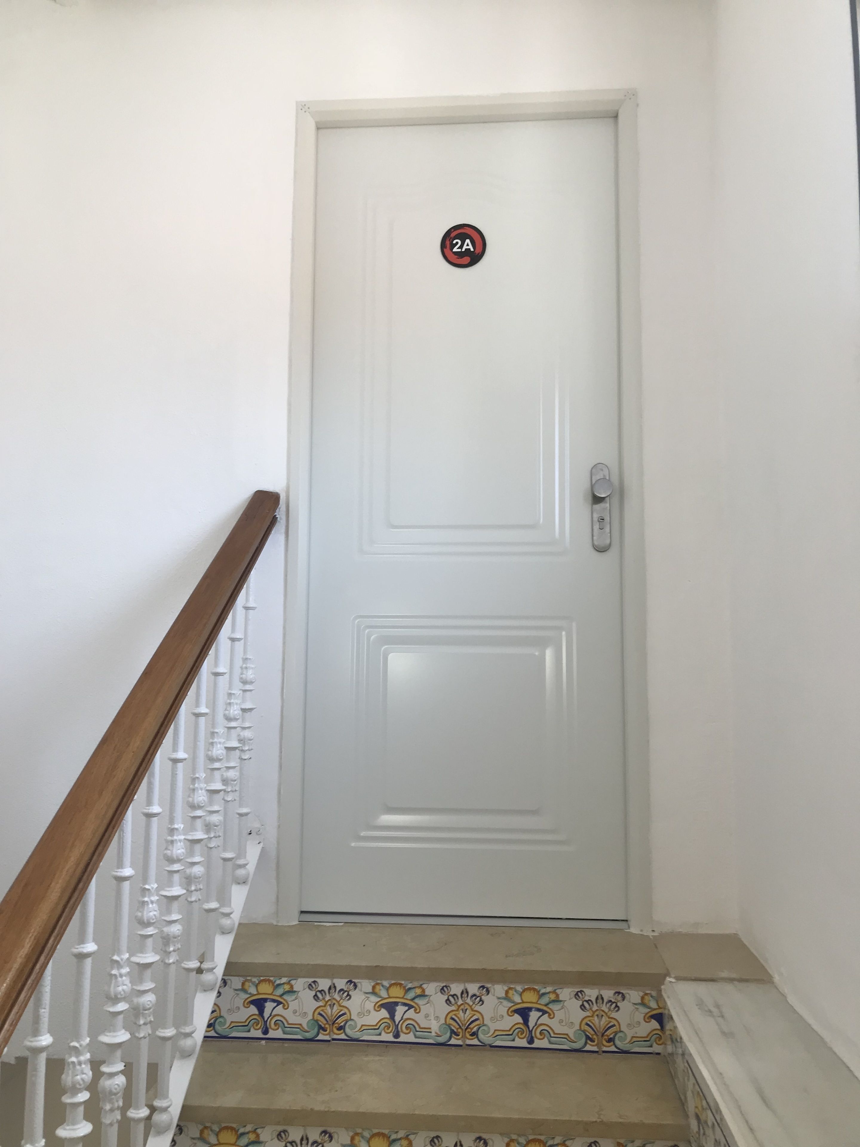 Eine weiße Tür mit einem '2A'-Schild, einem Holzhandlauf und einem gestreiften Fliesenboden.