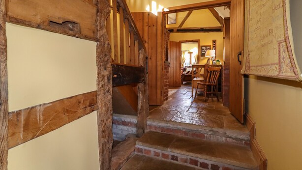 A rustic staircase with wooden beams and brick steps leading to a dining area with a table and chairs. - The Granary (Shrewsbury)
