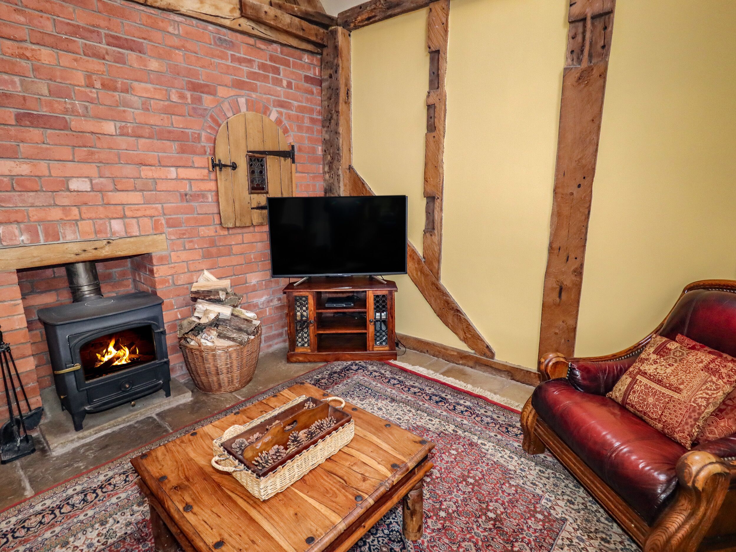 A cozy living room with a brick fireplace, a television, a leather sofa, and a wooden coffee table.