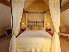 Una cama con dosel y cuatro columnas, con ropa de cama blanca y dos lámparas de noche.