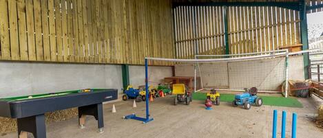 Un área de juegos cubierta en interior con mesa de billar, equipo de juegos infantiles y una portería de fútbol.