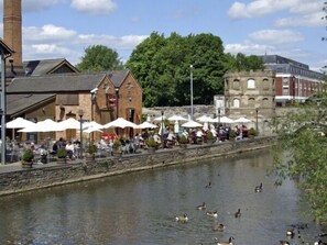 A riverside café with outdoor seating and ducks swimming in the water.