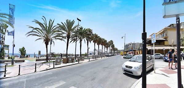 Una calle costera bordeada de palmeras y una playa al fondo.