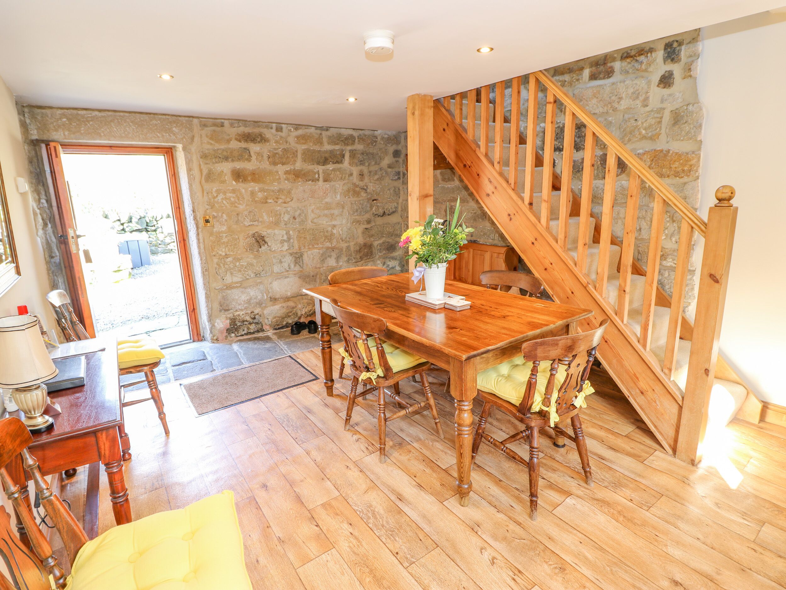 A dining area with a wooden table and chairs, a potted plant, and a staircase leading to an upper level.