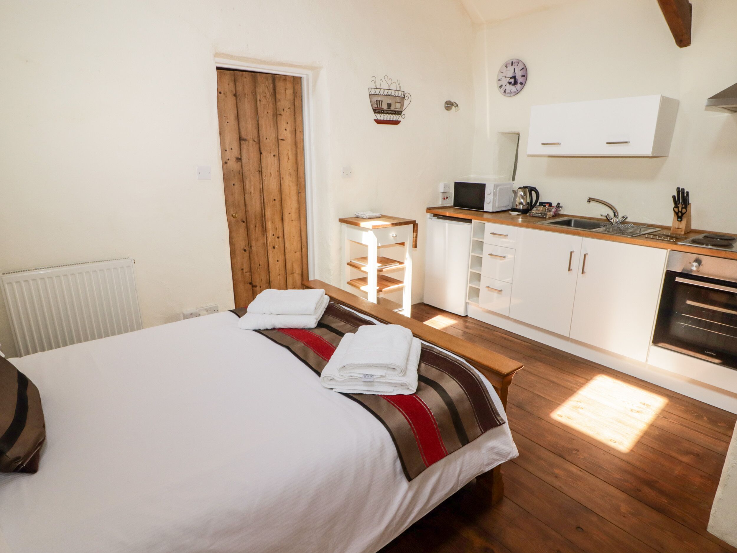 Une chambre avec un lit, une porte en bois, une petite kitchenette équipée d’un four à micro-ondes et d’un évier.