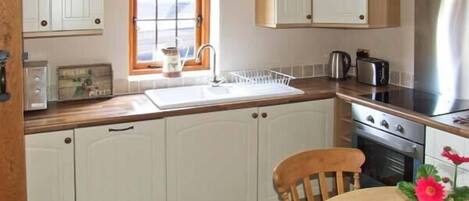 Una cocina con armarios blancos, encimera de madera, un lavabo, una estufa y una ventana con vistas.