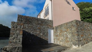 A stone staircase leading to a pink building with a white door, overlooking a body of water. - Curlew (Milford Haven)