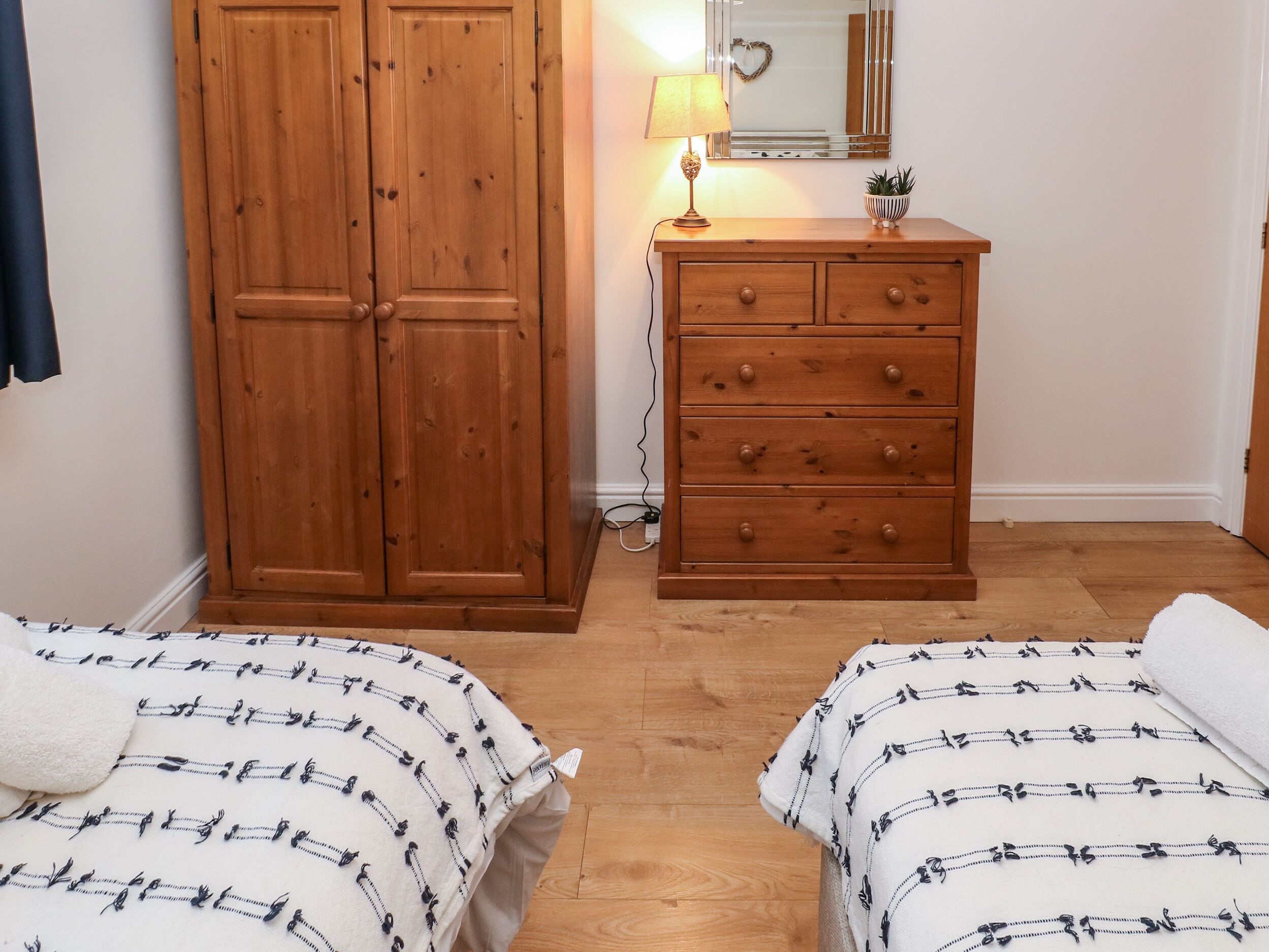 A bedroom with two beds, a wooden wardrobe, a dresser, a mirror, and a lamp.