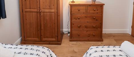 A bedroom with two beds, a wooden wardrobe, a dresser, a mirror, and a lamp.