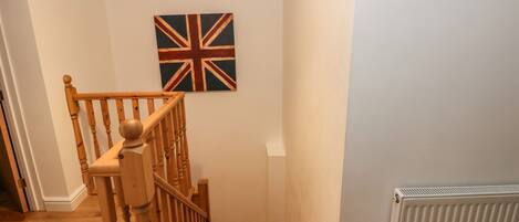 A staircase with wooden balusters and a handrail, leading to a landing with a wall-mounted flag.