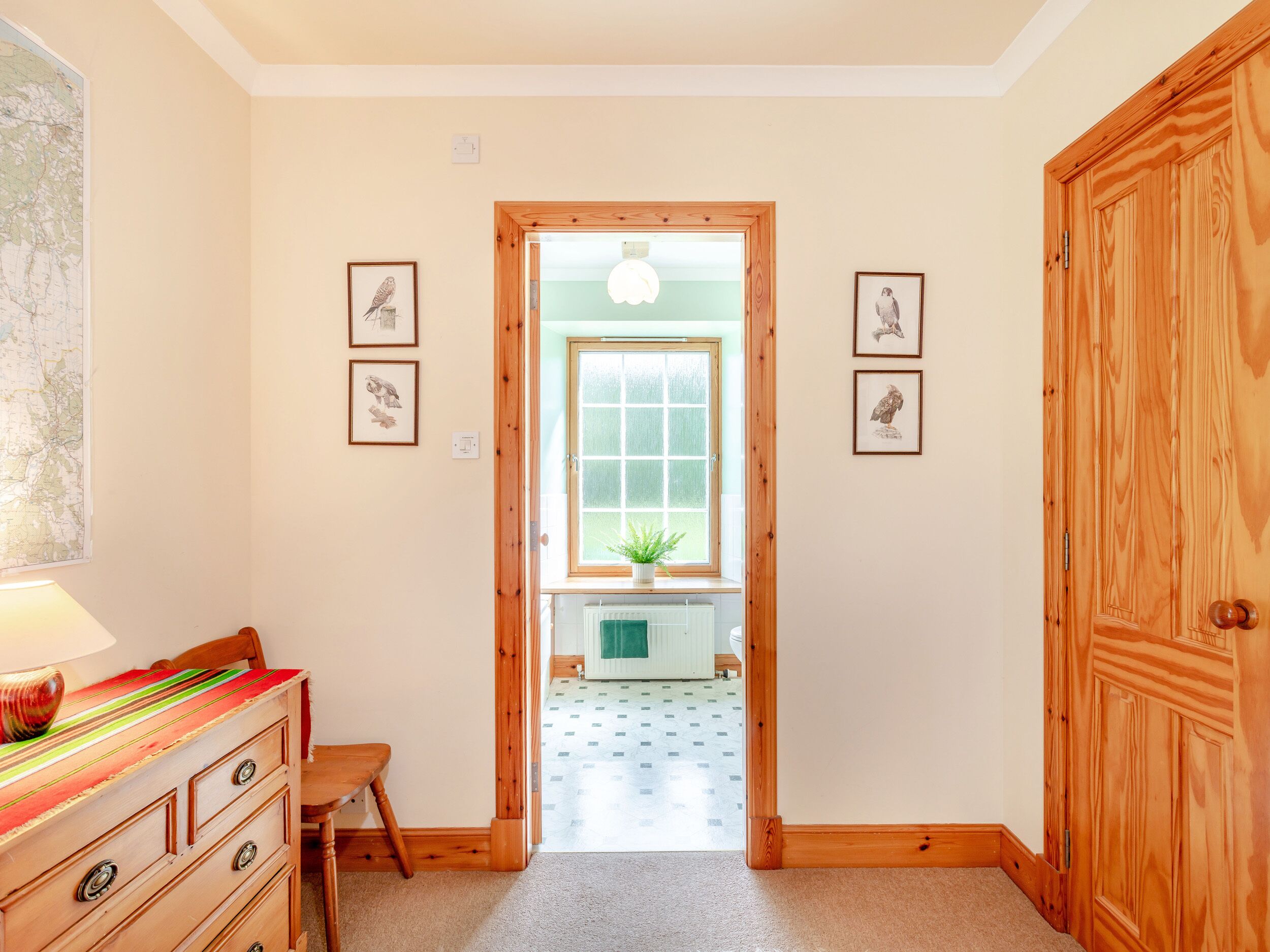 Un couloir avec des portes en bois, un bureau avec des tiroirs, une lampe et des tableaux encadrés accrochés aux murs.