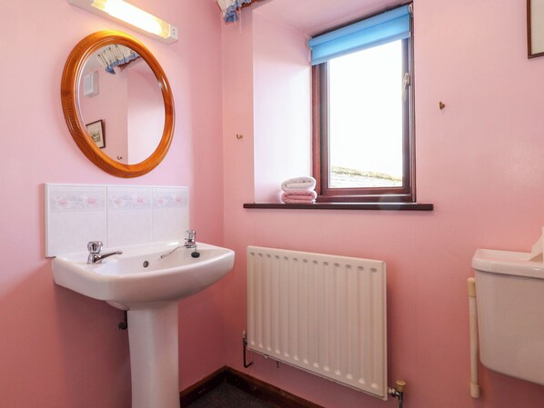 Un bany amb un lavabo blanc, un mirall, una finestra amb assecagorts i un radiador.