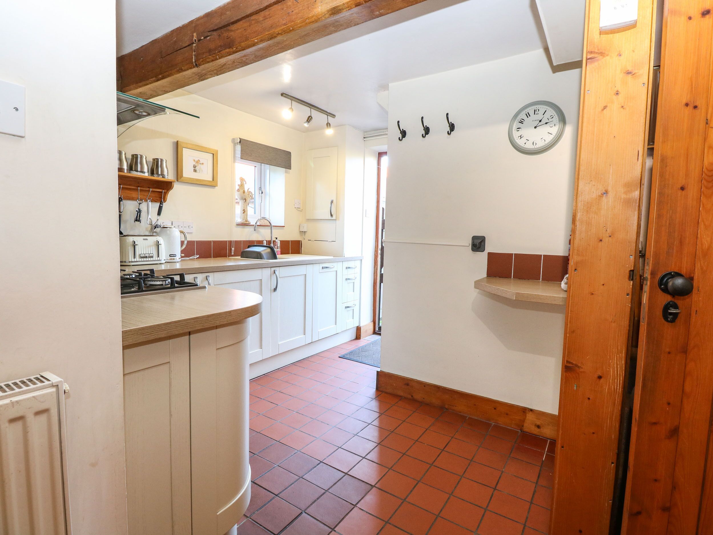 A kitchen with white cabinets, a wooden countertop, a stove, and a sink. There is a clock on the wall and a door with a wooden frame.