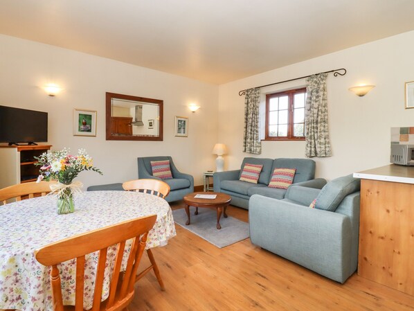 A cozy living room with a wooden dining table, two sofas, a TV, and a kitchen area. - Barn Owl Cottage (Woodbridge)