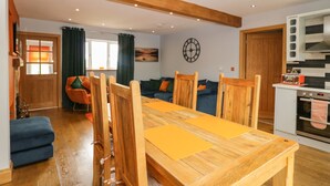 A dining area with a wooden table and chairs, a blue sofa, and a kitchen with a microwave and oven. - Bluebell Cottage (Ulverston)