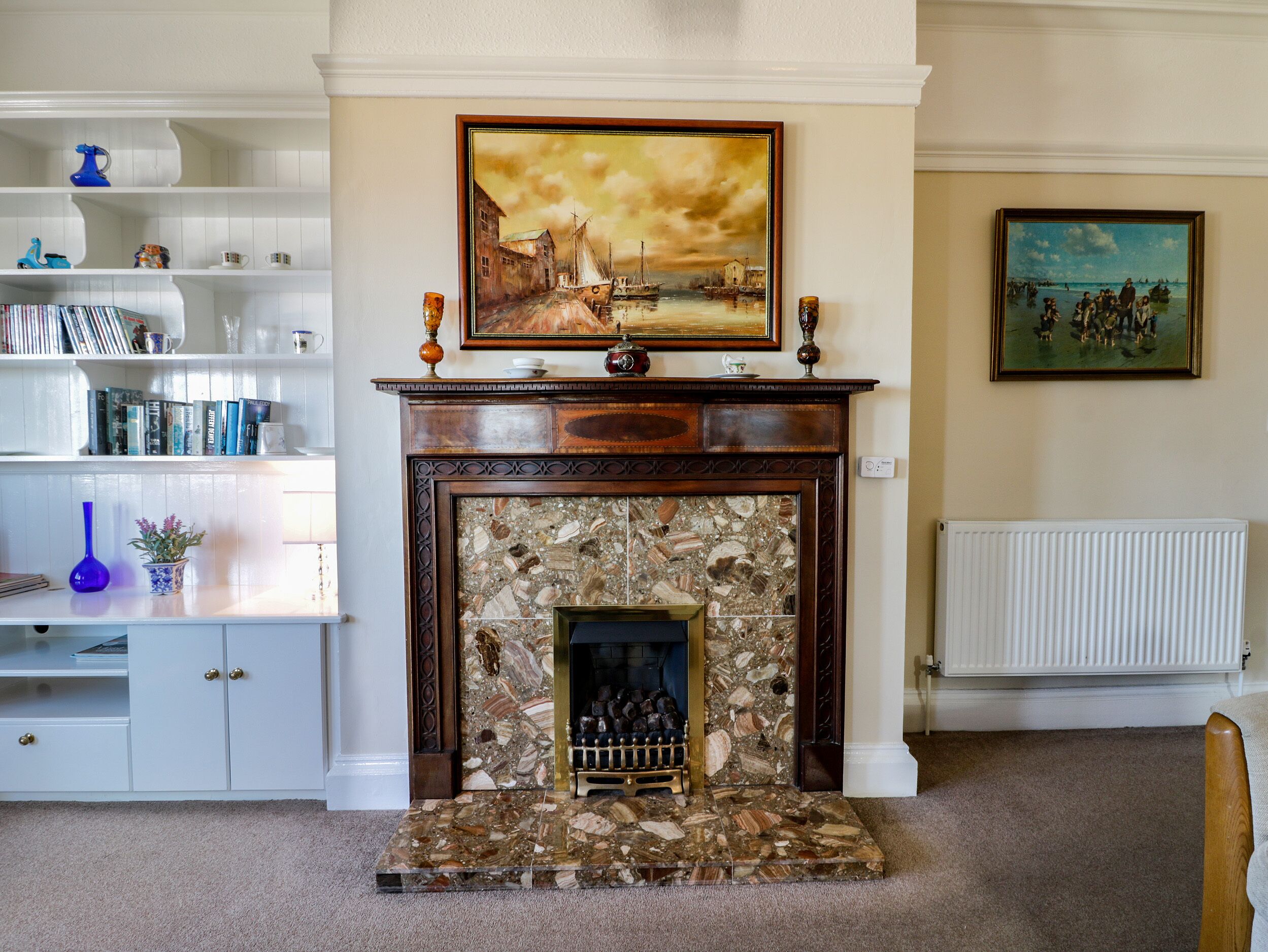 A living room with a fireplace, a bookshelf, and two paintings on the wall.