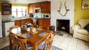 A cozy kitchen with wooden cabinets, a dining table with chairs, and a fireplace. - Kingsley Cottage (Norwich)