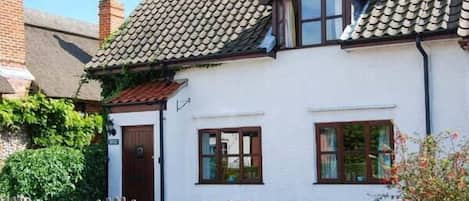 Een wit huis met pannendak, houten ramen en een houten omheining.