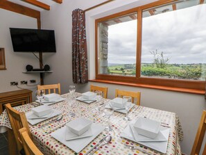 Un coin repas avec une table dressée pour quatre personnes, un téléviseur fixé au mur et une fenêtre donnant sur la campagne.