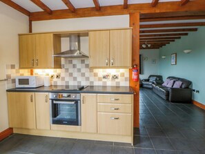 A compact kitchen with wooden cabinets, a microwave, an oven, and a checkered backsplash. - Y Bwthyn (Tregaron)