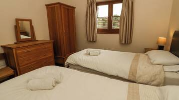 A bedroom with two beds, a wooden dresser, a mirror, and a window with curtains.