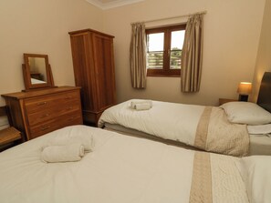 A bedroom with two beds, a wooden dresser, a mirror, and a window with curtains. - Y Bwthyn (Tregaron)