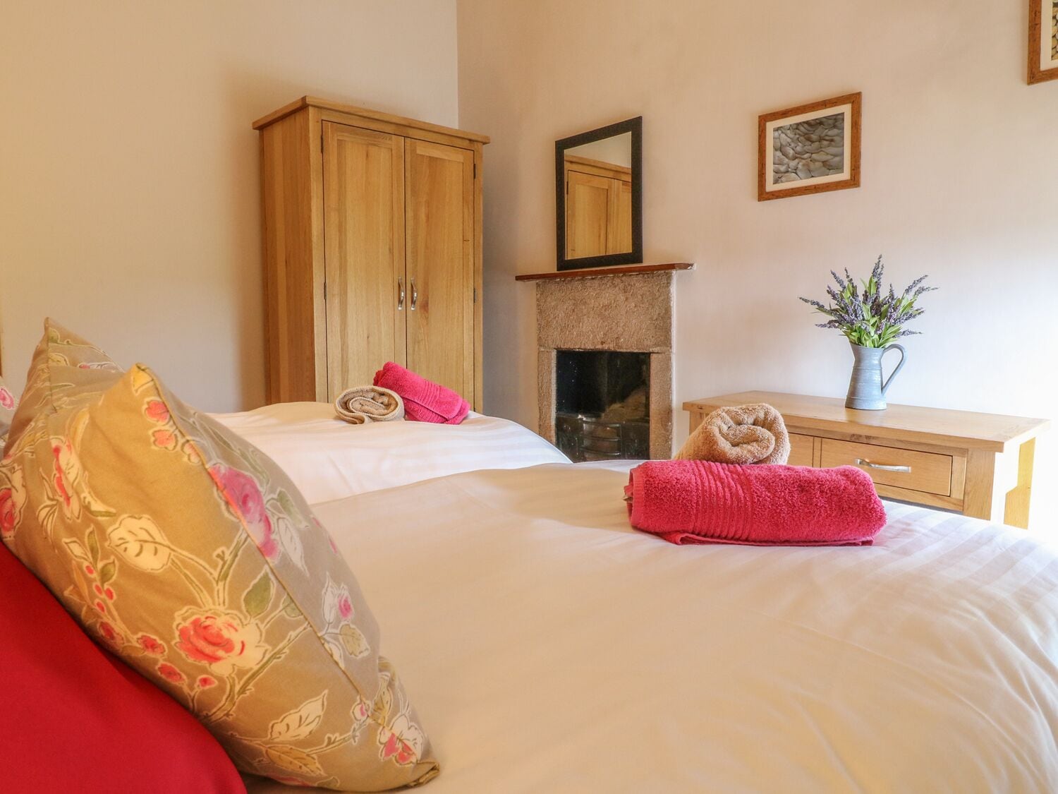 Un dormitorio con cama, un armario de madera, chimenea y un jarrón con flores.