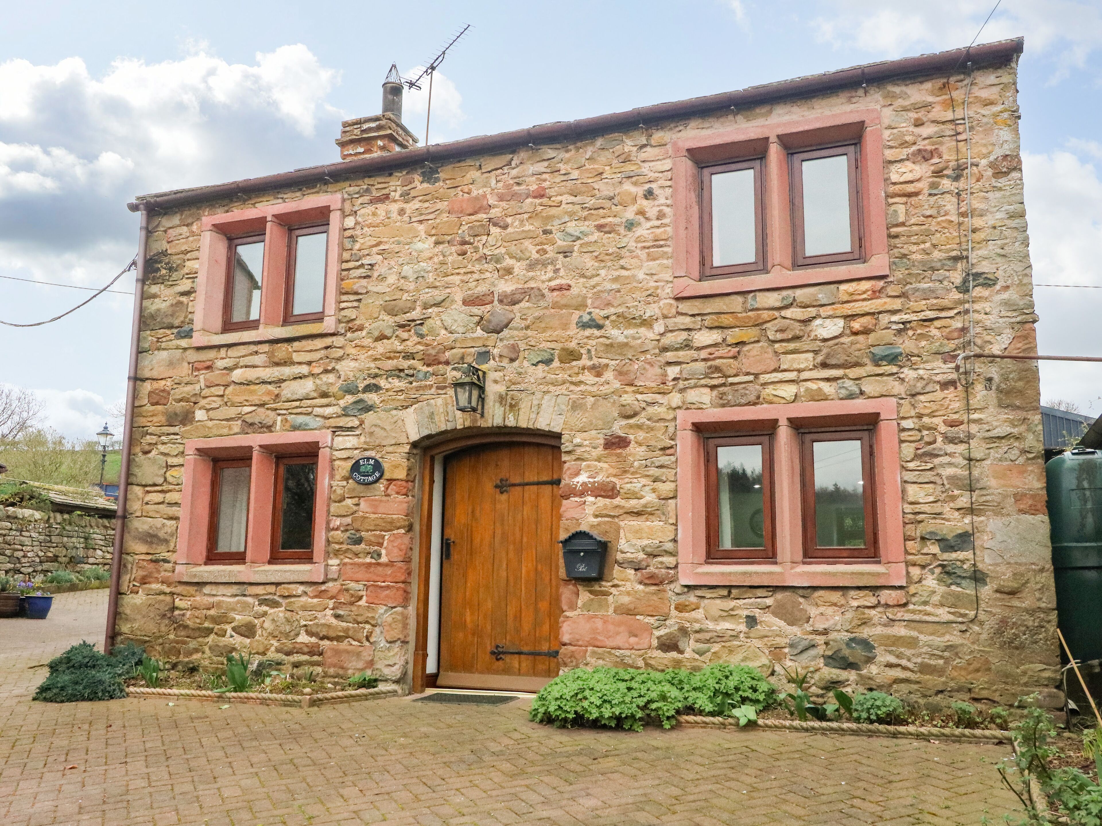 Une petite maison en pierre avec une porte en bois, deux fenêtres avec volets et un petit jardin.