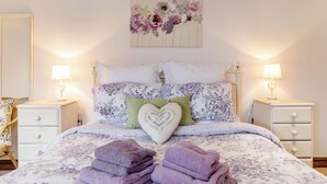 A neatly made bed with floral bedding, a heart-shaped pillow, and two bedside lamps. - Willow Cottage (Driffield)